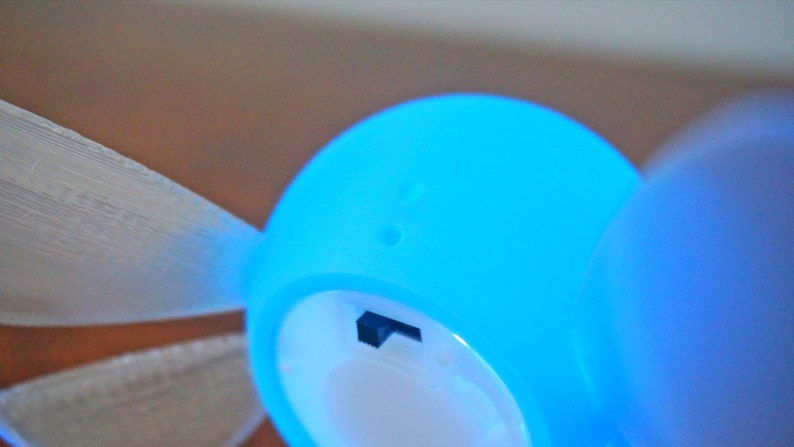 May include: A blue and white light-up fairy figurine with wings. The fairy has a small hole on the top of its head and a small black switch on the side.