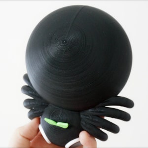 May include: Black and green 3D printed spider figurine with a round head and eight legs.