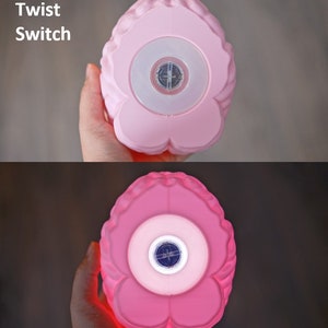 May include: A pink, flower-shaped night light with a twist switch. The light has a central circular area with a compass-like design. The text "Twist Switch" is visible. The light glows red when turned on.