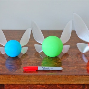 May include: Four different sized, 3D printed, white fairy wings with a sphere attached to the back. The spheres are pink, blue, green, and red.