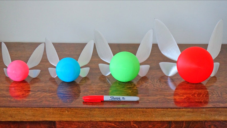 May include: Four different sized, 3D printed, white fairy wings with a sphere attached to the back. The spheres are pink, blue, green, and red.