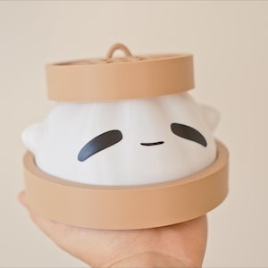 Puede incluir: Una luz nocturna de cer&aacute;mica blanca con forma de bola de masa con una base marr&oacute;n y una linda cara de dibujos animados. La luz tiene la forma de una bola de masa china tradicional.