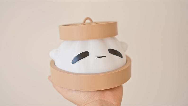 Puede incluir: Una luz nocturna de cer&aacute;mica blanca con forma de bola de masa con una base marr&oacute;n y una linda cara de dibujos animados. La luz tiene la forma de una bola de masa china tradicional.