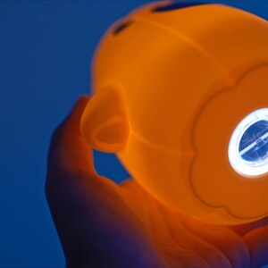 May include: A bright orange nightlight shaped like a face with a white light shining through a flower-shaped opening.