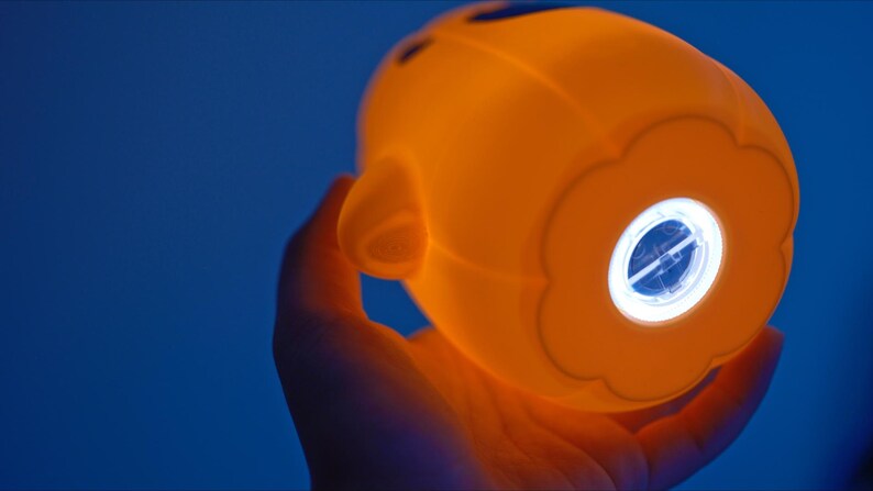May include: A bright orange nightlight shaped like a face with a white light shining through a flower-shaped opening.
