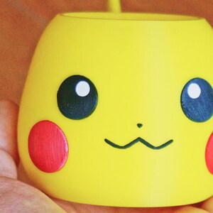 May include: A yellow ceramic planter shaped like Pikachu, a popular Pokemon character. The planter has black eyes, a red nose, and a black mouth.