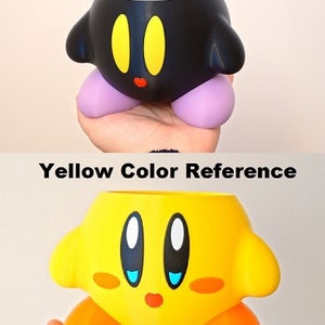 Puede incluir: Dos macetas impresas en 3D con forma del personaje Kirby de la serie de videojuegos Kirby. La maceta de arriba es negra con ojos amarillos y una boca roja. La maceta de abajo es amarilla con ojos negros, pupilas blancas, p&aacute;rpados azules y pies naranjas.