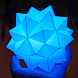 Peut inclure: Une étoile en papier géométrique bleue avec un design 3D. L'étoile est éclairée de l'intérieur, créant un effet lumineux.