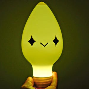 May include: A cheerful, yellow lightbulb with a cartoon face. The bulb has a teardrop shape and a standard base. The face features two black diamond-shaped eyes and a small, curved mouth. The light is bright.