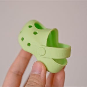 May include: A light green silicone shoe charm with a strap and holes.