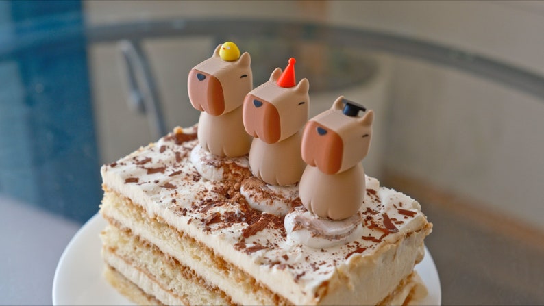 May include: A multi-layered cake with a white frosting and chocolate sprinkles. Three small brown figurines with different hats are on top of the cake.