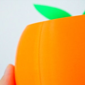 May include: Orange ceramic planter with a green leaf design. The planter is made of a smooth, glossy material.