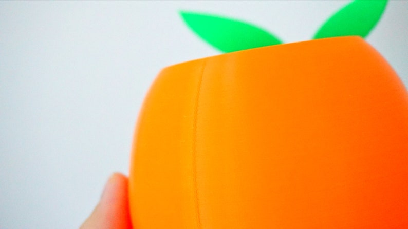 May include: Orange ceramic planter with a green leaf design. The planter is made of a smooth, glossy material.