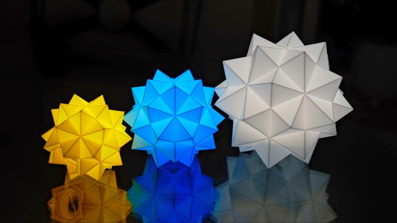 Pode incluir: Tr&ecirc;s estrelas de papel geom&eacute;tricas em tamanhos diferentes. A maior estrela &eacute; branca, a estrela do meio &eacute; azul e a menor estrela &eacute; amarela.