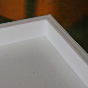 May include: Close-up of a white frame with a textured surface. The frame is made of a thick, sturdy material and has a clean, modern design.