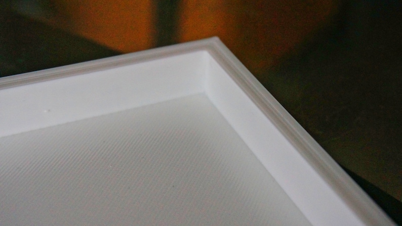 May include: Close-up of a white frame with a textured surface. The frame is made of a thick, sturdy material and has a clean, modern design.