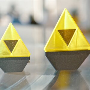 May include: Two yellow plastic Triforce figurines with black bases. The larger figurine is about 3 inches tall and the smaller figurine is about 2 inches tall.