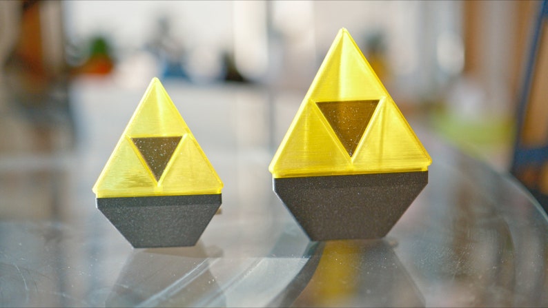 May include: Two yellow plastic Triforce figurines with black bases. The larger figurine is about 3 inches tall and the smaller figurine is about 2 inches tall.