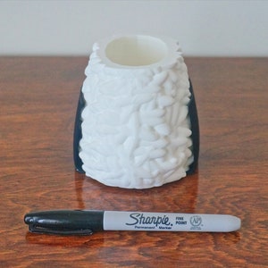 Puede incluir: Un jarr&oacute;n de cer&aacute;mica blanco con base negra y un dise&ntilde;o texturizado org&aacute;nico. El jarr&oacute;n est&aacute; sobre una superficie de madera con un marcador permanente negro Sharpie punta fina delante de &eacute;l.