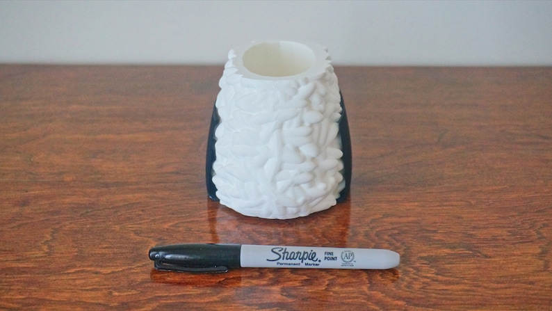 Puede incluir: Un jarr&oacute;n de cer&aacute;mica blanco con base negra y un dise&ntilde;o texturizado org&aacute;nico. El jarr&oacute;n est&aacute; sobre una superficie de madera con un marcador permanente negro Sharpie punta fina delante de &eacute;l.