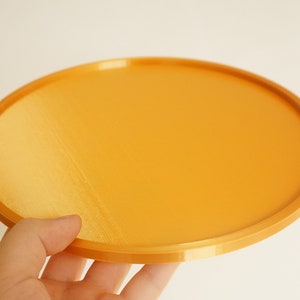 May include: A round, orange tray made of plastic. The tray has a smooth, slightly textured surface.