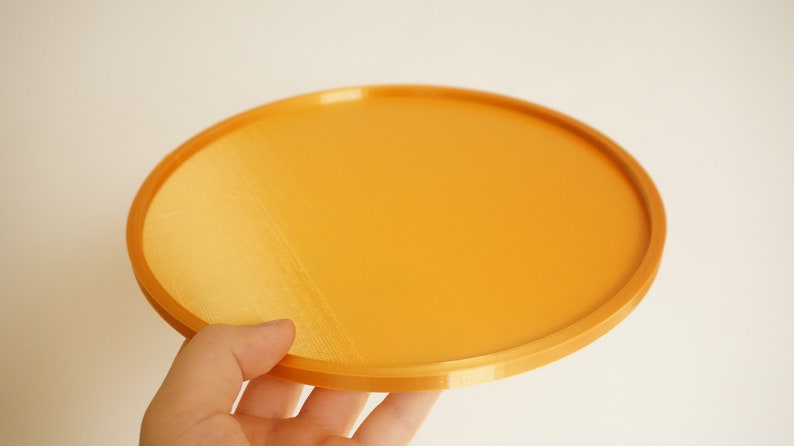 May include: A round, orange tray made of plastic. The tray has a smooth, slightly textured surface.