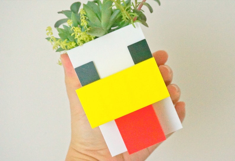 May include: A white ceramic planter shaped like a chicken with black eyes, a yellow beak, and a red wattle. The planter is filled with green succulents.
