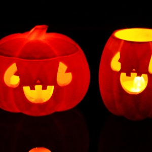 May include: Two orange jack-o'-lantern pumpkins with carved faces and lit candles inside. The pumpkins are on a black background.