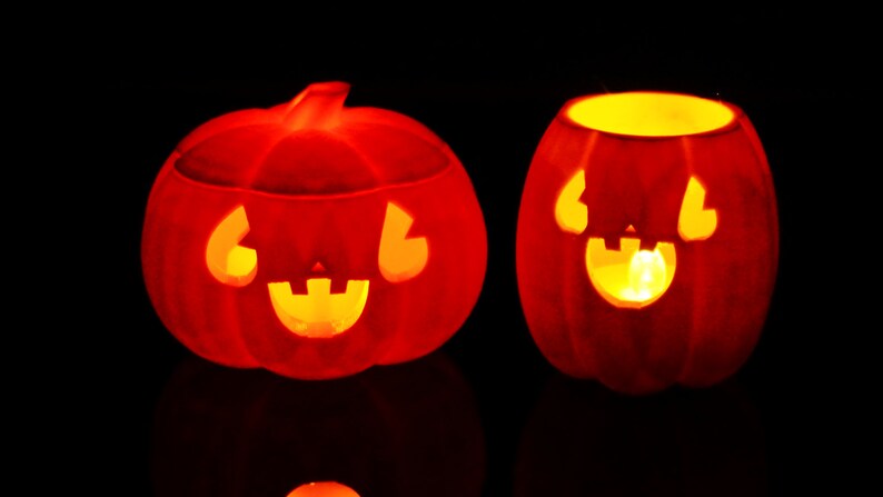 May include: Two orange jack-o'-lantern pumpkins with carved faces and lit candles inside. The pumpkins are on a black background.