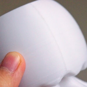 May include: White ceramic planter with a smooth, rounded shape. The planter has a seam down the side.
