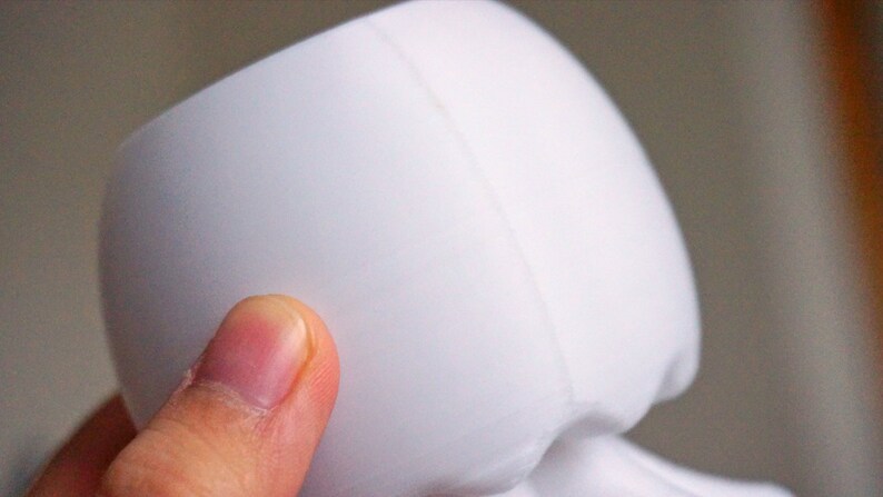 May include: White ceramic planter with a smooth, rounded shape. The planter has a seam down the side.