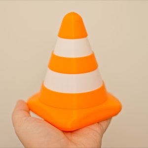 Op de afbeelding: Een kleine oranje en witte verkeerskegel met een vierkante basis.