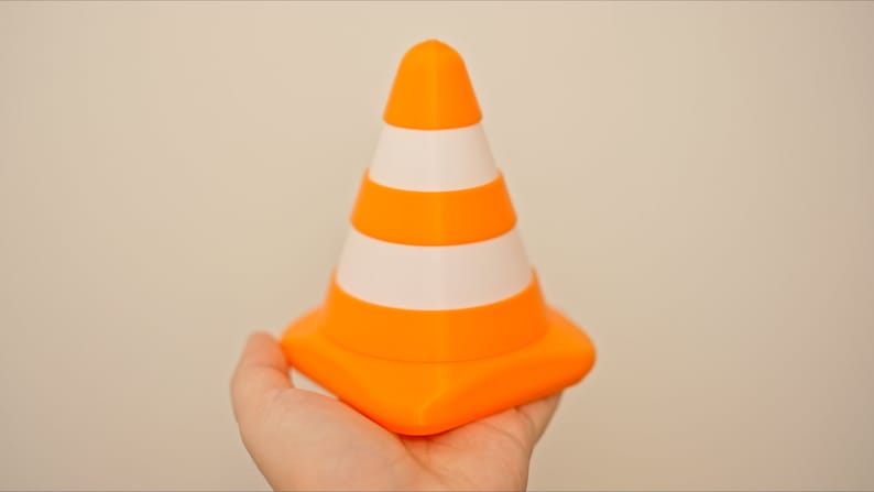 Op de afbeelding: Een kleine oranje en witte verkeerskegel met een vierkante basis.