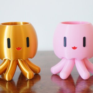 May include: Two 3D printed octopus planters, one gold and one pink, with a cute cartoon face and eight tentacles.