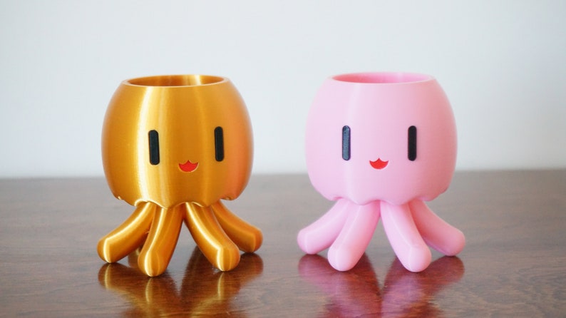 May include: Two 3D printed octopus planters, one gold and one pink, with a cute cartoon face and eight tentacles.