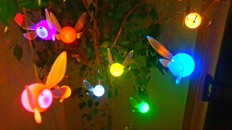 May include: A string of fairy lights shaped like the iconic video game character, the fairy, with glowing multi-colored bulbs. The lights are hanging from a tree branch.