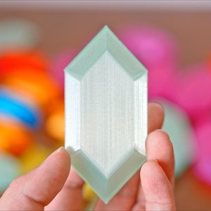 May include: A light green, 3D printed, geometric shape resembling a crystal. The shape has a smooth, textured surface and is held in a hand.