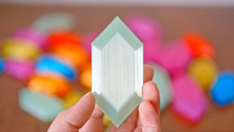 May include: A light green, 3D printed, geometric shape resembling a crystal. The shape has a smooth, textured surface and is held in a hand.