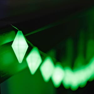 May include: A string of diamond-shaped, glowing green lights against a dark background. The lights are in focus in the foreground, with a blurred trail of lights extending into the distance. The overall effect is a vibrant, festive display.