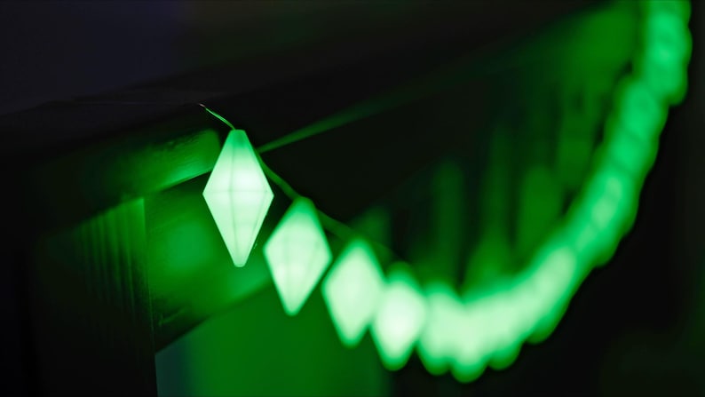 May include: A string of diamond-shaped, glowing green lights against a dark background. The lights are in focus in the foreground, with a blurred trail of lights extending into the distance. The overall effect is a vibrant, festive display.