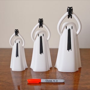 Peut inclure: Trois figurines de fant&ocirc;mes blanches avec des figurines de chats noirs sur la t&ecirc;te. Les fant&ocirc;mes sont de tailles diff&eacute;rentes et sont dispos&eacute;s par ordre de taille du plus petit au plus grand. Les fant&ocirc;mes ont des yeux et une bouche noirs. Les figurines sont sur une surface en bois.