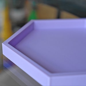 May include: A light purple hexagonal tray with a raised edge. The tray is made of a smooth, textured material.