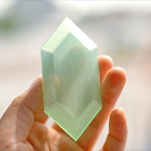 May include: A translucent green plastic replica of a video game item, shaped like a diamond.