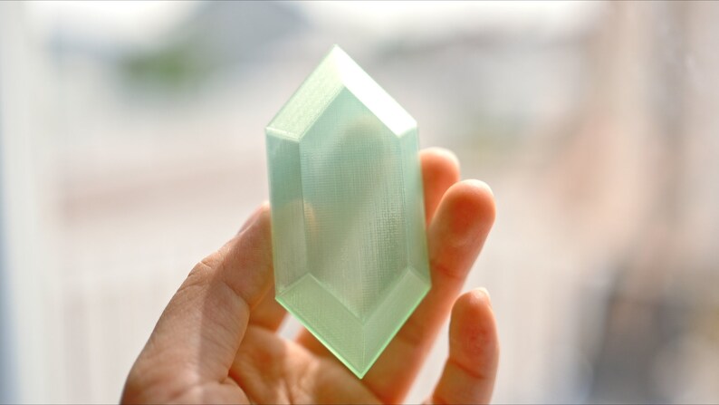 May include: A translucent green plastic replica of a video game item, shaped like a diamond.