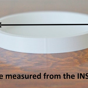 May include: White round cake pan with a measurement line across the inside.  Size measured from the INSIDE.