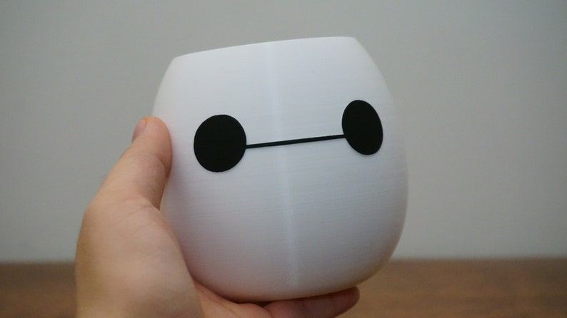 Pu&ograve; includere: Vaso da fiori in ceramica bianca a forma di personaggio dei cartoni animati con occhi neri e una linea nera per la bocca.