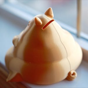 May include: A light brown ceramic piggy bank with a slot on the back for coins. The piggy bank is shaped like a pig with a curled tail and a snout.