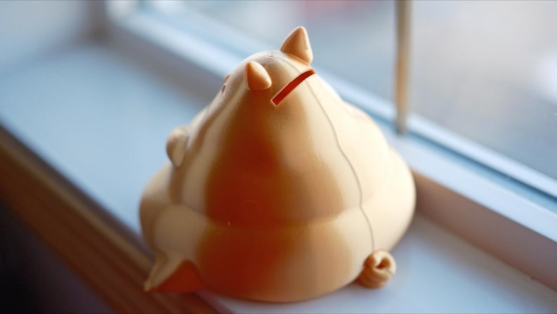 May include: A light brown ceramic piggy bank with a slot on the back for coins. The piggy bank is shaped like a pig with a curled tail and a snout.