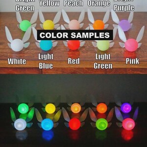 May include: A collection of colorful fairy light ornaments, each with a glowing orb and translucent wings. The image displays color samples, including white, light blue, red, and pink, with the text "COLOR SAMPLES" displayed.