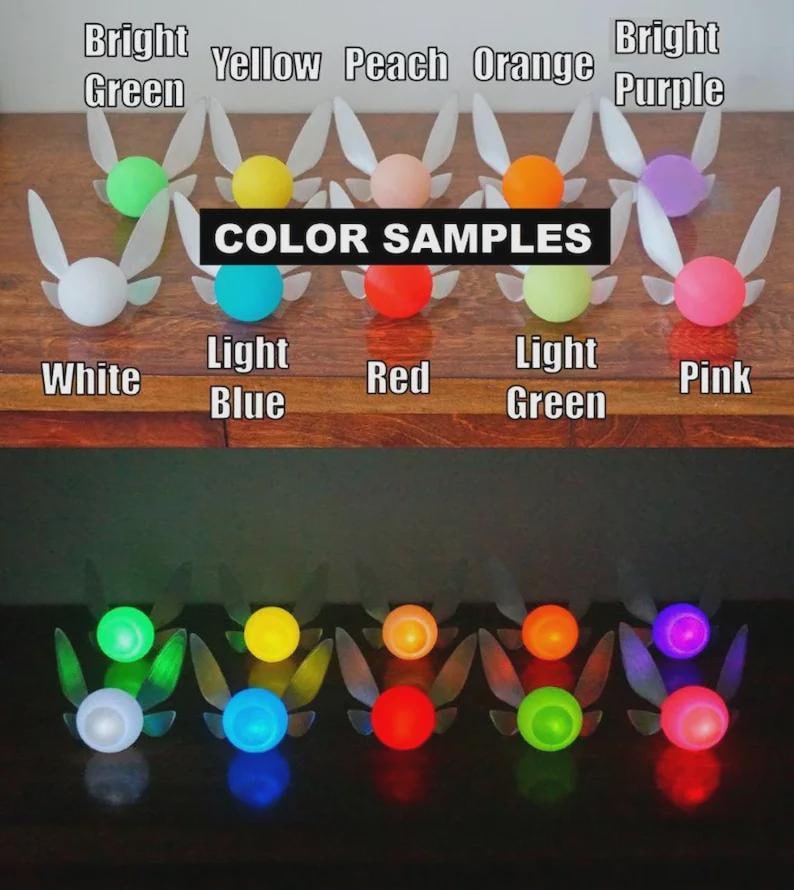 May include: A collection of colorful fairy light ornaments, each with a glowing orb and translucent wings. The image displays color samples, including white, light blue, red, and pink, with the text "COLOR SAMPLES" displayed.